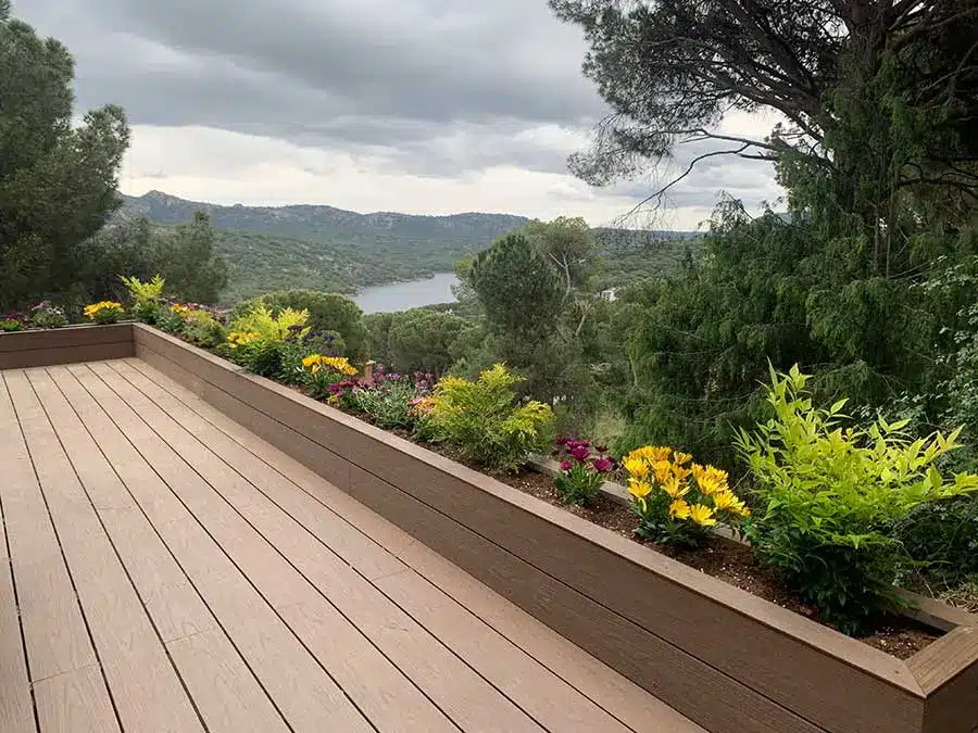 Tarima de composite marrón en terraza con jardinera Tarima de composite en tono marrón en una terraza con jardinera integrada y vistas a la sierra