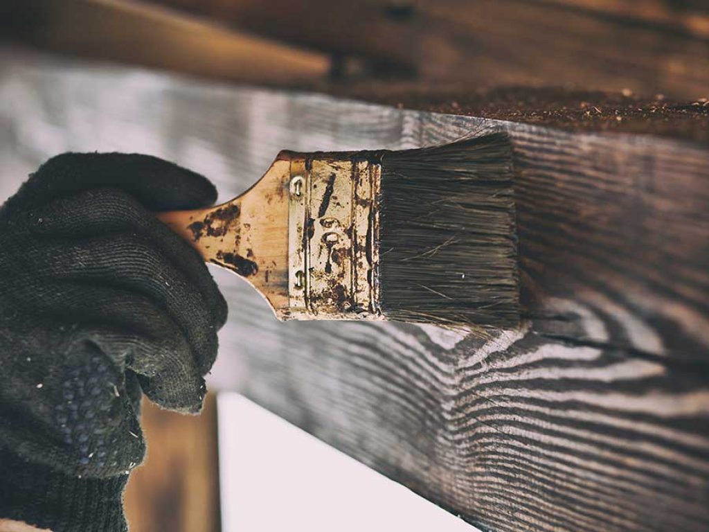 Trabajador aplicando un lasur protector a una estructura de madera.