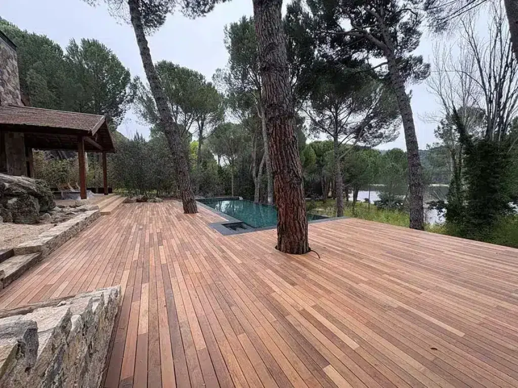 Tarima de madera de ipé junto a una piscina, con el tronco de un pino integrado en el suelo